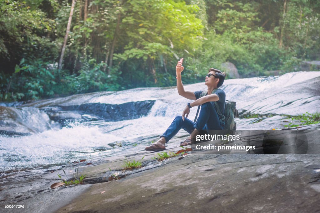 Hiker with backpack and laptop and phone at  waterfall  the forest.