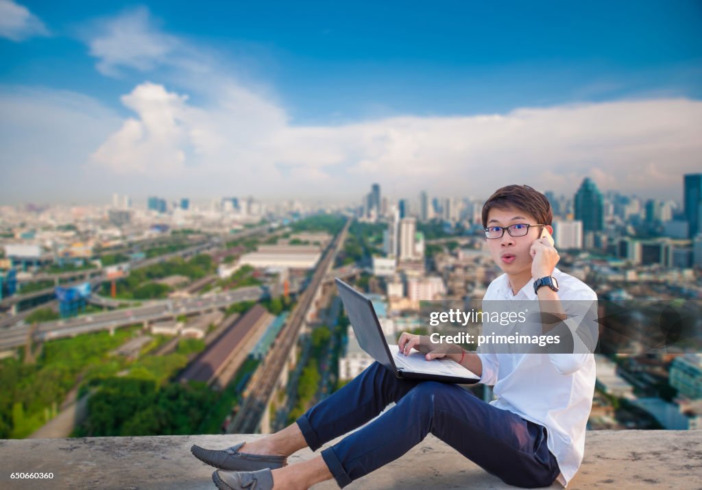 Young business man using laptop and digital tablet cityscape background