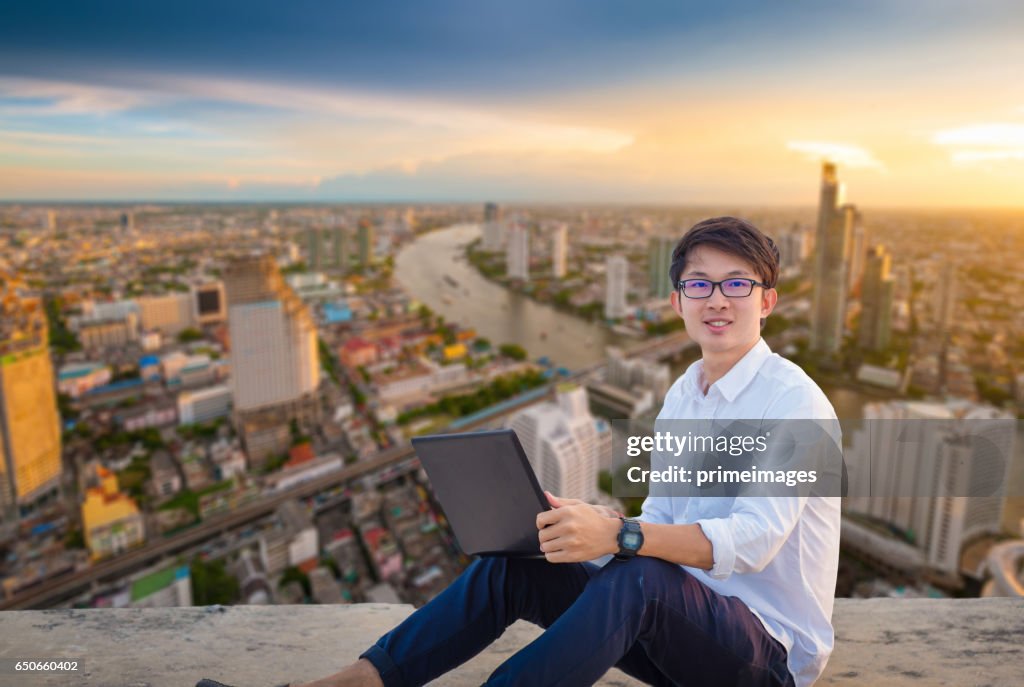 Young business man using laptop and digital tablet cityscape background