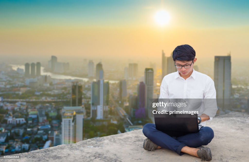 Young business man using laptop and digital tablet cityscape background