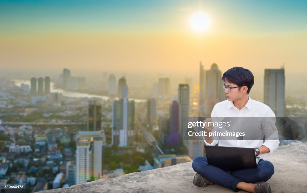 Young business man using laptop and digital tablet cityscape background