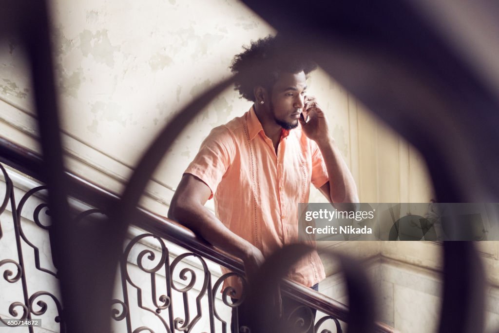 Young man answering smart phone while standing on steps at home