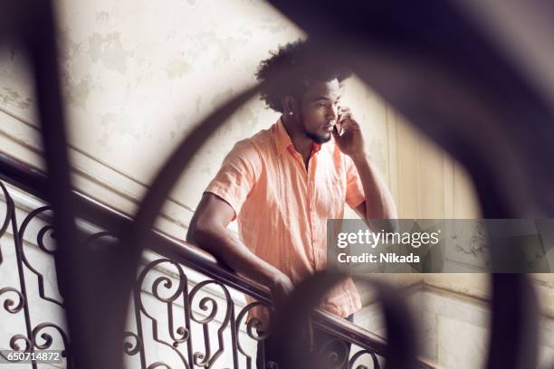 young man answering smart phone while standing on steps at home - cuban ethnicity stock pictures, royalty-free photos & images