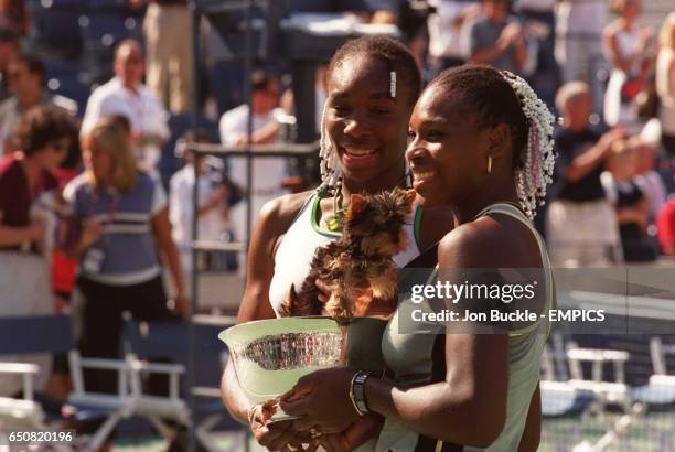 Venus and Serena Williams celebrate with the women's doubles trophy containing their pet puppy, Jackie