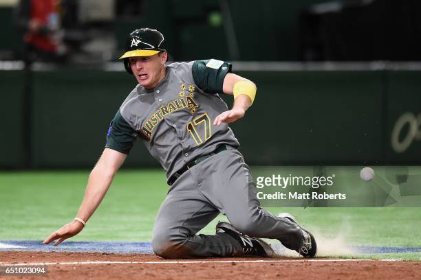 Outfielder Mitch Dening of Australia slides safely into the home plate to score a run by a RBI single of Infielder Logan Wade of Australia to make it...