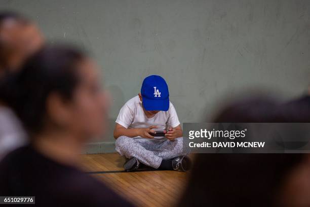 Boy wears a Los Angeles logo cap and plays an electronic game at a workshop for immigrants to make a preparedness plan, in case they are confronted...