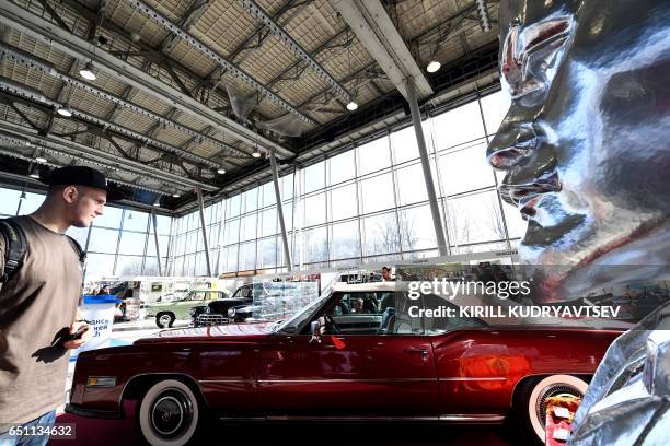 Man looks at a Cadillac Eldorado car of 1975 displayed next to a bust of Soviet Union's founder Vladimir Lenin as they visit an exhibition of 50 old...