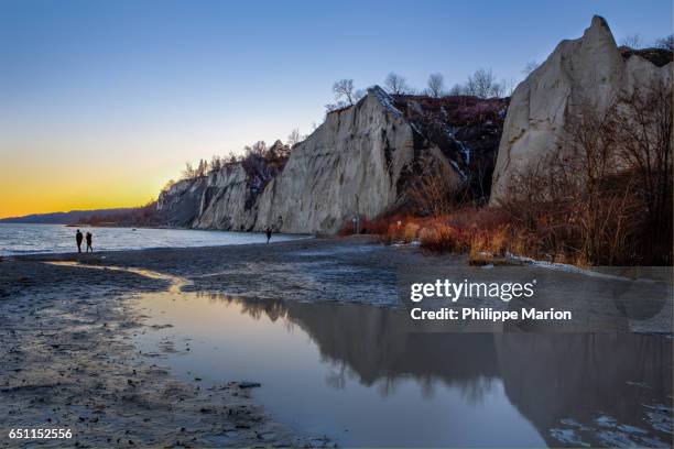 after sunset on a cold winter day a silhouetted couple walks by lake ontario and scarborough bluffs, toronto - ontariosee stock-fotos und bilder