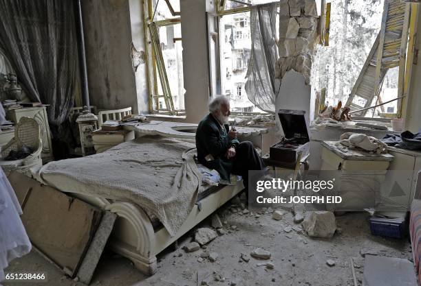 Mohammed Mohiedin Anis, or Abu Omar smokes his pipe as he sits in his destroyed bedroom listening to music on his vinyl player, gramophone, in...