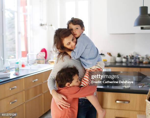 a mom hugging her sons in the kitchen - familia con dos hijos fotografías e imágenes de stock