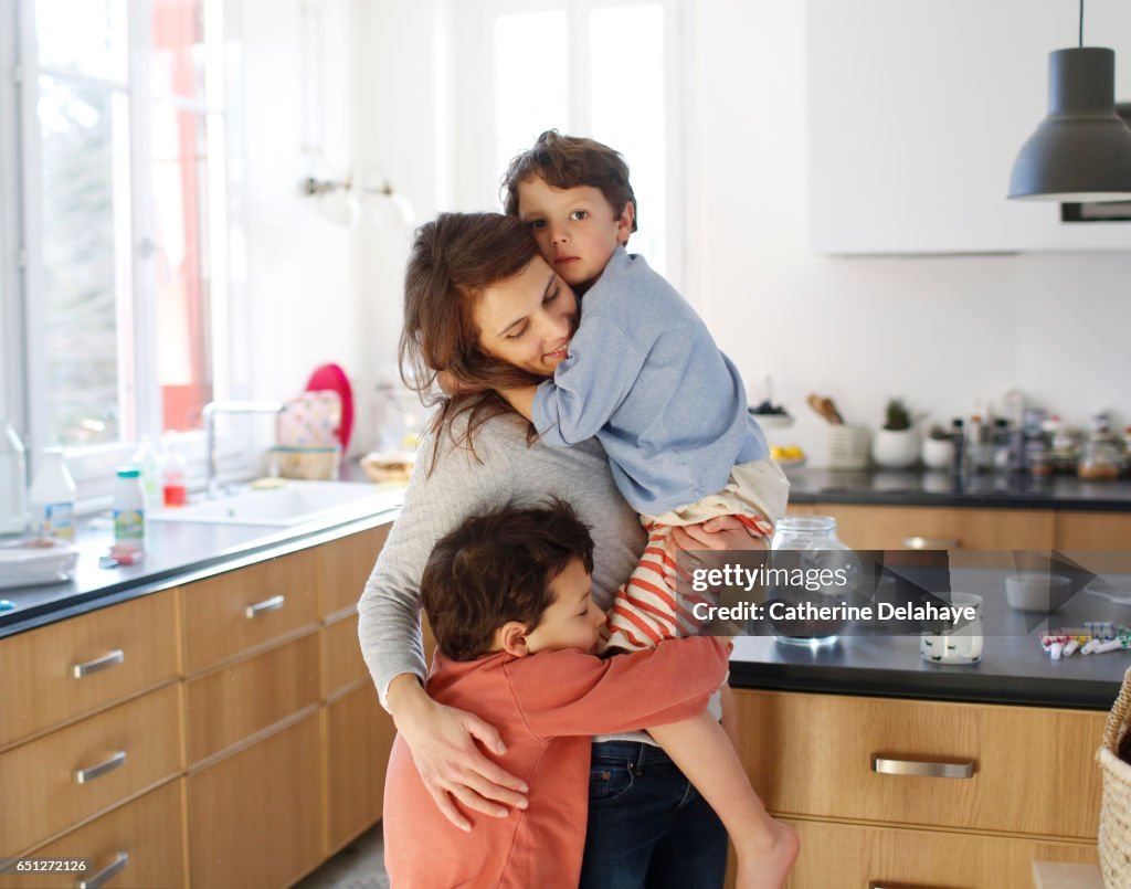 A mom hugging her sons in the kitchen