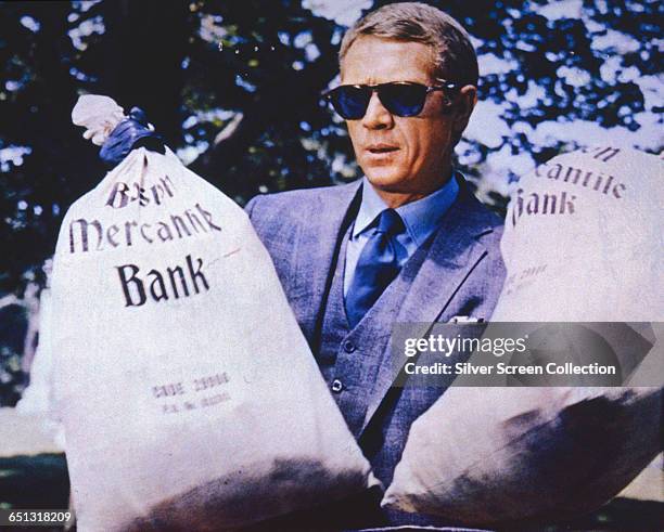 American actor Steve McQueen as the titular thief, holding two sacks from the Boston Mercantile Bank in a scene from the heist film 'The Thomas Crown...
