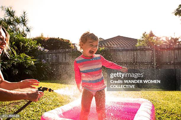 young girl splashing hose and pool and sunflare - kinder am wasser stock-fotos und bilder