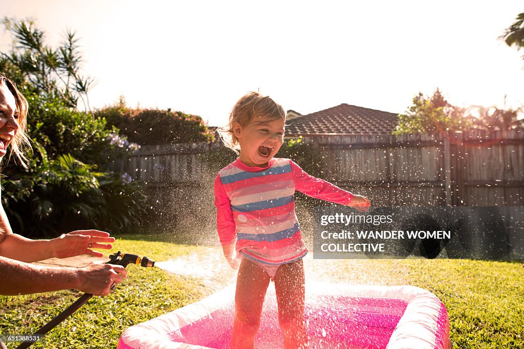 Young girl splashing hose and pool and sunflare