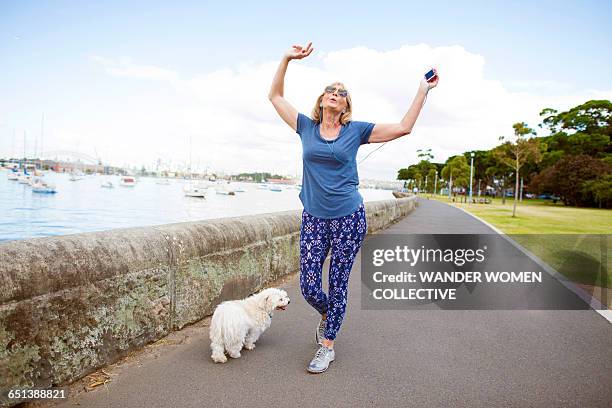 mature woman with dog and mp3 dancing on street - alzar los brazos fotografías e imágenes de stock