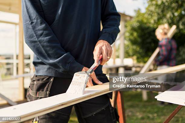 man painting wooden plank while woman assisting in background - shed stockfoto's en -beelden