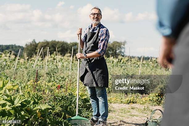 mature farmer holding gardening fork and standing with coworker at farm - tuinvork stockfoto's en -beelden