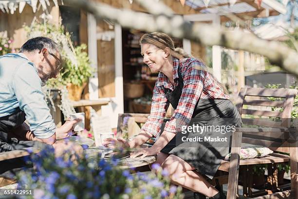 sales clerks discussing while sitting on chairs against food store - bioladen stock-fotos und bilder