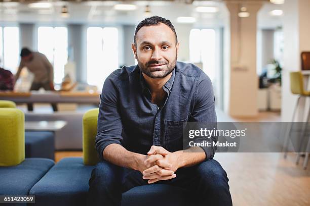 portrait of mid adult man with hands clasped relaxing on couch at corridor - office portrait uomo foto e immagini stock