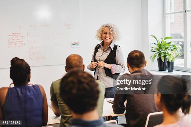 smiling teacher talking to multi-ethnic students at language class - adult classroom stock pictures, royalty-free photos & images