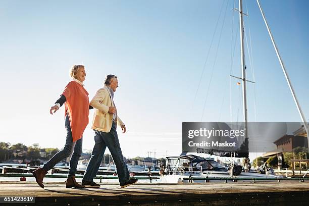 full length of happy senior couple walking on pier against sky - aangemeerd stockfoto's en -beelden