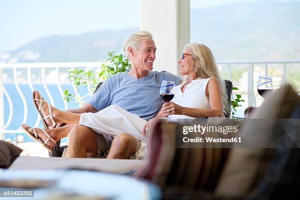 happy senior couple with glass of red wine in home by the sea - beach house balcony fotografías e imágenes de stock