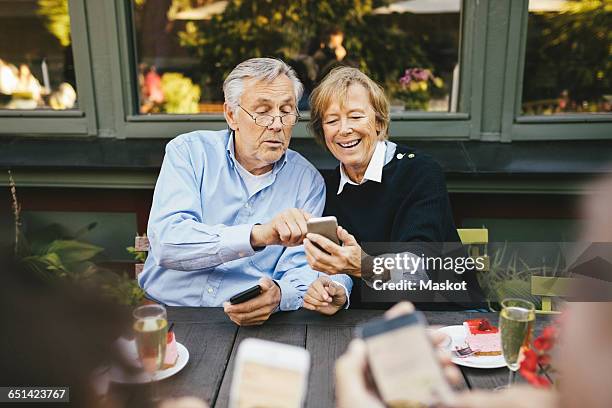 happy senior couple using mobile phone at outdoor restaurant - senior women cafe stock pictures, royalty-free photos & images