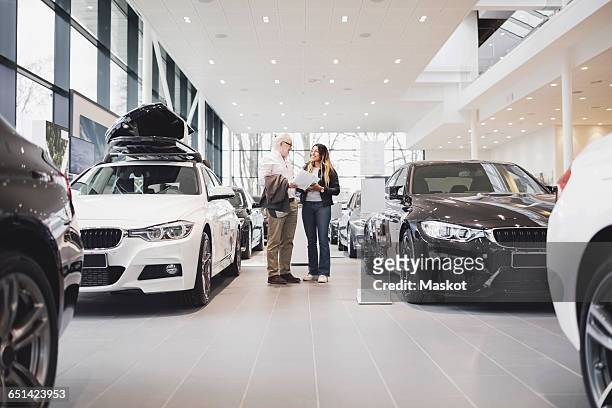 man and woman with paper standing amidst cars at showroom - salone d'esposizione foto e immagini stock
