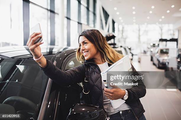 smiling woman taking selfie with new car in showroom - selective focus imagens e fotografias de stock