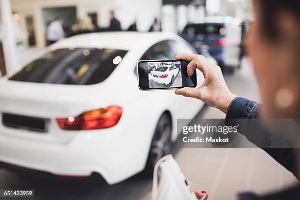 senior woman photographing new car through mobile phone at showroom - car mobile stockfoto's en -beelden