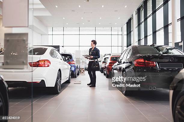 senior woman holding documents and looking at cars in showroom - car dealership imagens e fotografias de stock