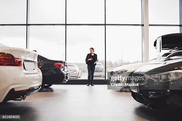 full length of woman standing amidst cars in showroom - kaufen stock-fotos und bilder