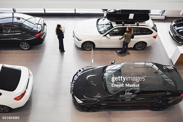 high angle view of saleswoman and customer looking at car in showroom - bilförsäljare bildbanksfoton och bilder