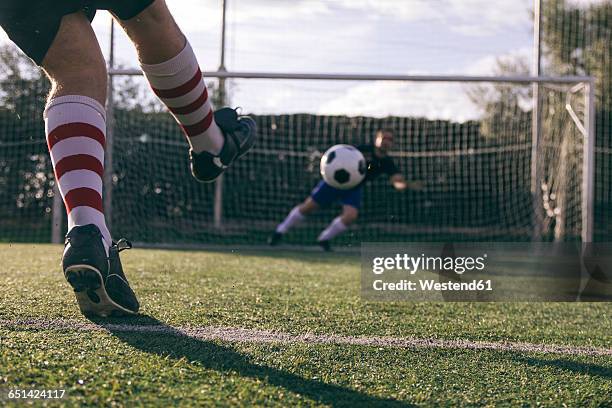 legs of a footnball player kicking a ball in front of a goal with a goalkeeper - porta calcio foto e immagini stock
