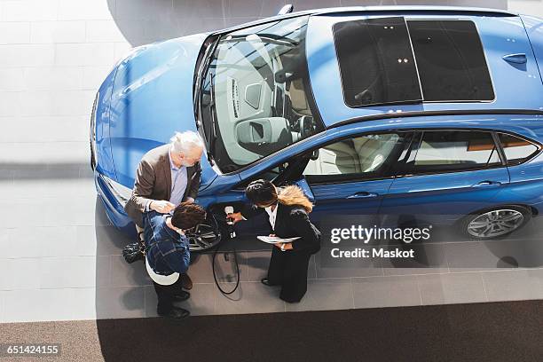 saleswoman explaining customers to charge electric car at showroom - old man looking down stock pictures, royalty-free photos & images