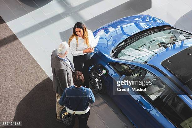 high angle view of saleswoman showing car to customers at showroom - kaufen stock-fotos und bilder