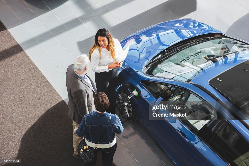High angle view of saleswoman showing car to customers at showroom