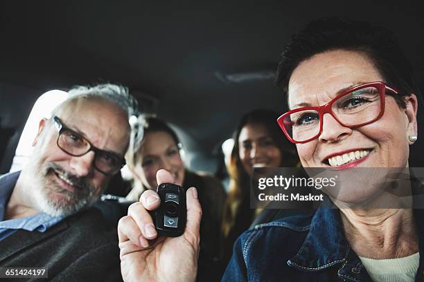 smiling senior woman holding remote while sitting with people in car - four people in car fotografías e imágenes de stock