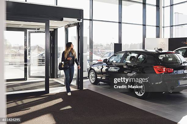 full length of young woman entering car showroom - salone d'esposizione foto e immagini stock