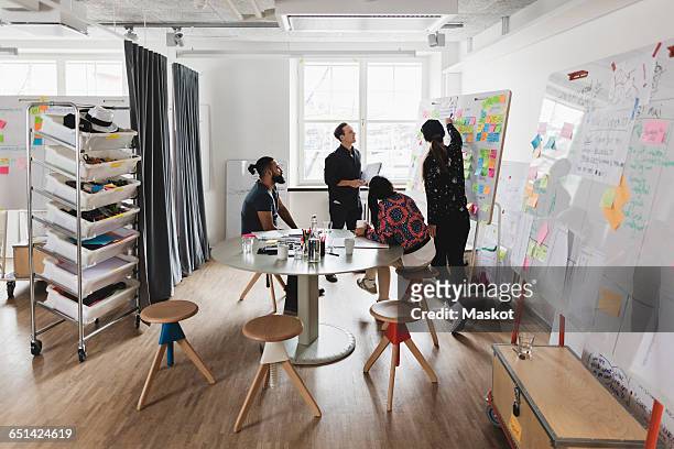 businesswoman showing colleagues note on whiteboard during meeting in board room - creative occupation stock-fotos und bilder