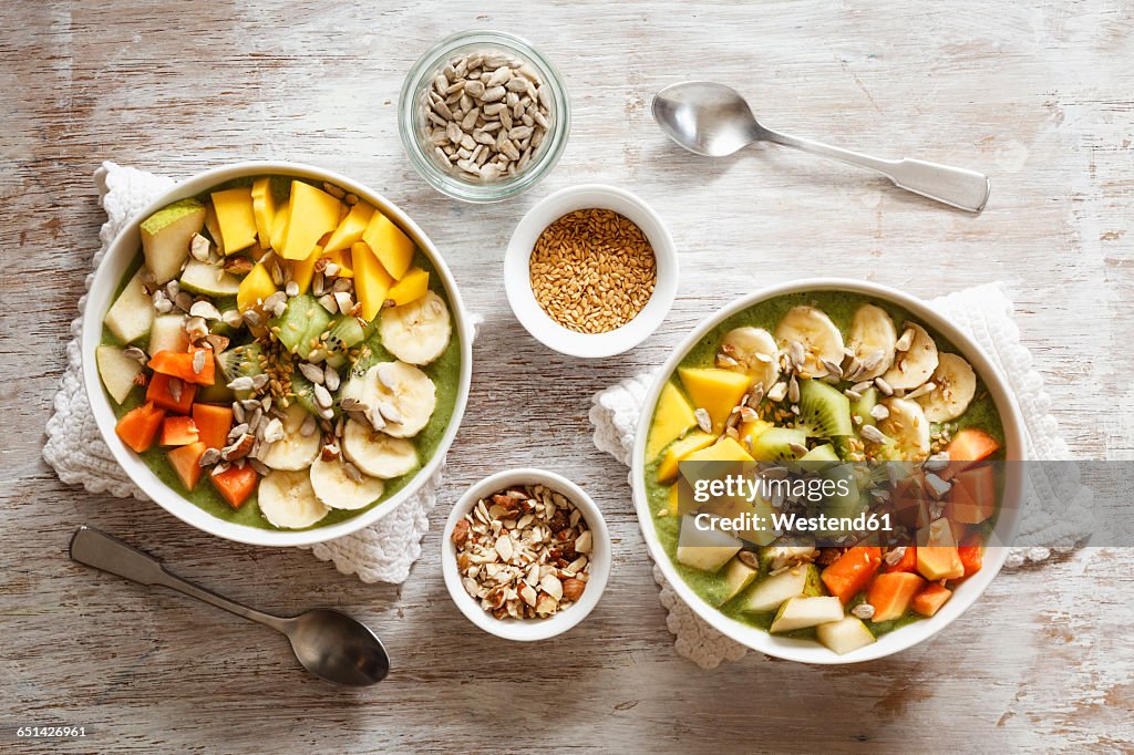 Smoothie bowl with different fruits, mango, papaya, kiwi, banana and pear and toppings, lineseeds, sunflower-seeds and nuts