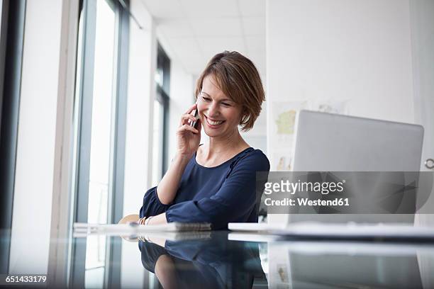 smiling businesswoman on cell phone at office desk - businesswoman talking smartphone stock-fotos und bilder