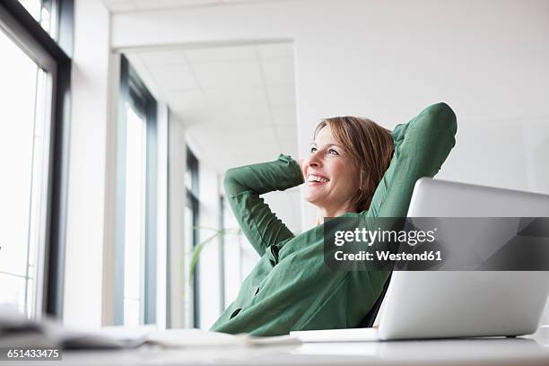 smiling businesswoman at office desk leaning back - daydreaming woman stock-fotos und bilder