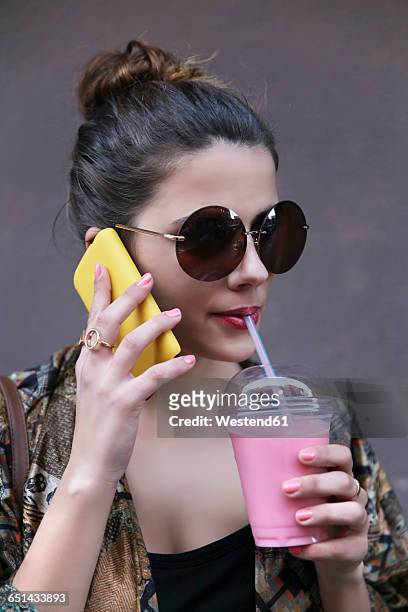 portrait of young woman drinking smoothie while telephoning with smartphone - straw lips stock pictures, royalty-free photos & images