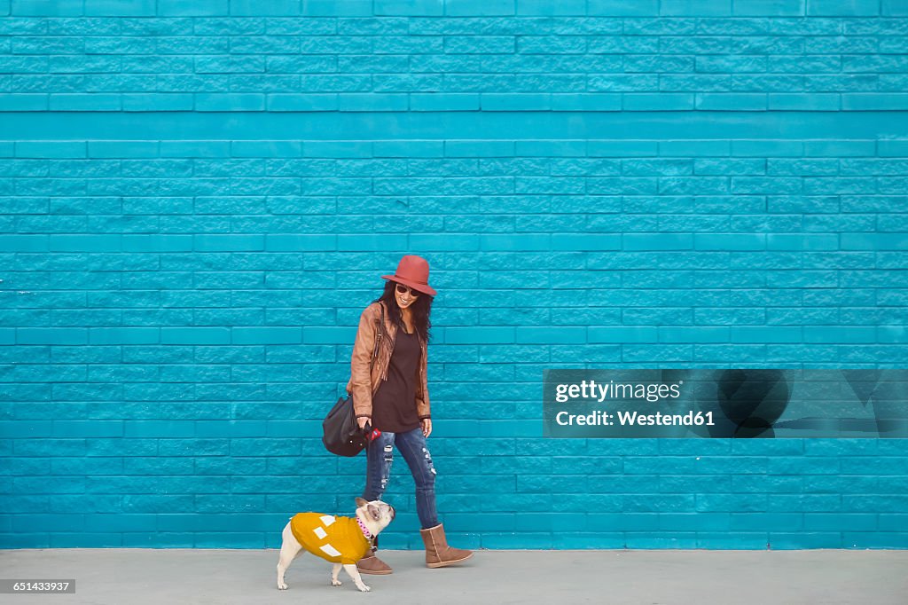 Woman going walkies with her French bulldog in front of blue wall