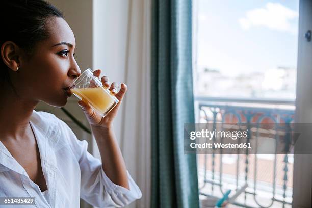 young woman drinking glass of juice while looking through window - orange juice stockfoto's en -beelden