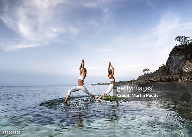 young women practicing yoga at seashore - ankle deep in water - fotografias e filmes do acervo