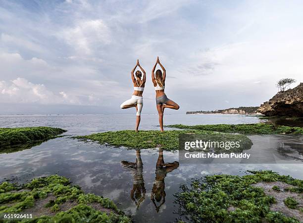 young women practicing yoga at seashore - standing water stockfoto's en -beelden