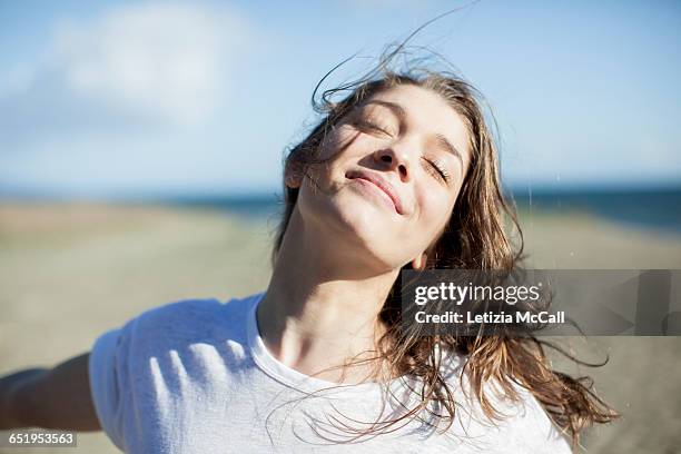 young woman with eyes closed smiling on a beach - alegre fotografías e imágenes de stock