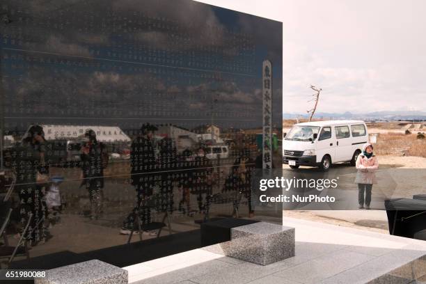 People look for the name of their relatives and friends from the memorial monument for the victims of massive earthquake and tsunami disaster in...